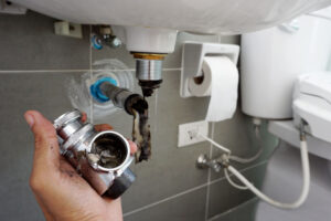 Bingham Plumbing & Gas - Close-up of hand holding a clogged sink drainage pipe filled with dirt and debris.